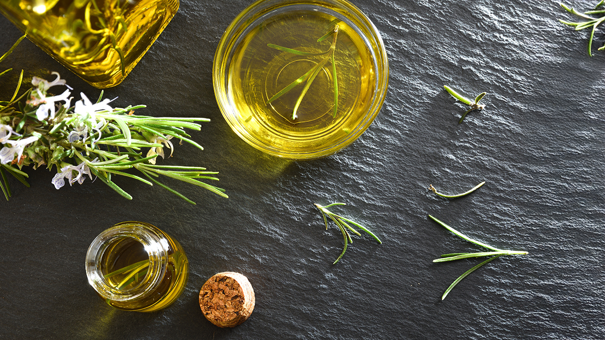Rosemary hair oil for growth in glass jars and rosemary tips on a rough gray stone surface